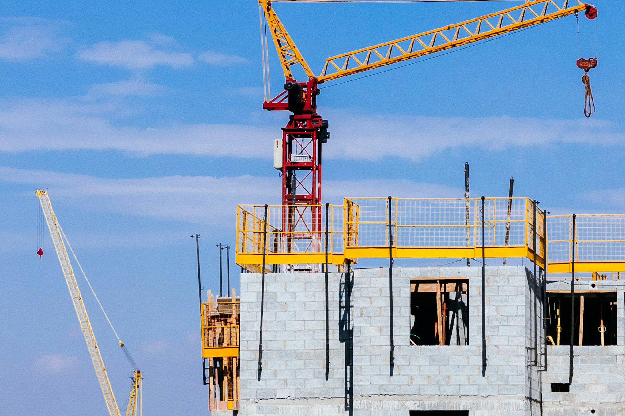 Tower cranes at a construction site working on a high-rise building under a clear blue sky.